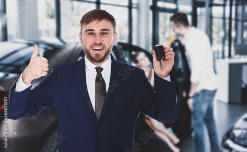 Happy salesman with key in car salon