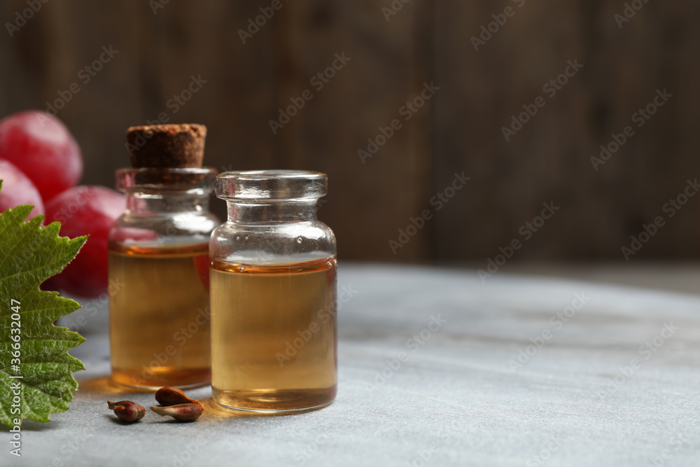 Bottles of natural grape seed oil on grey table, space for text. Organic cosmetic