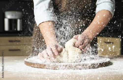 Fotografia Young woman kneading dough at table in kitchen, closeup