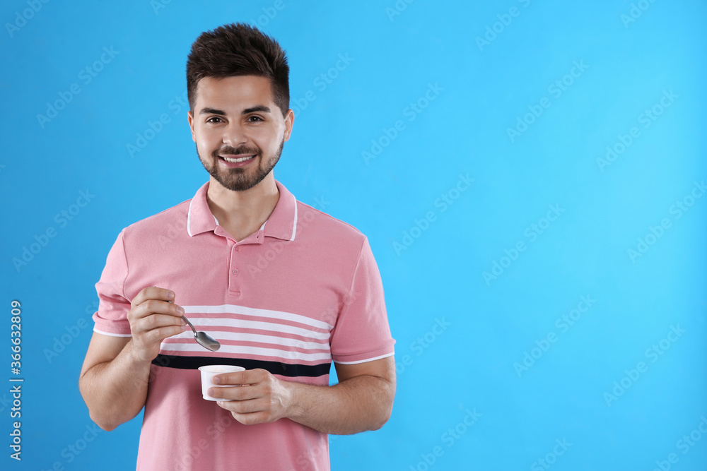 Happy young man with yogurt and spoon on light blue background. Space for text Happy young man with yogurt and spoon on light blue background. Space for text