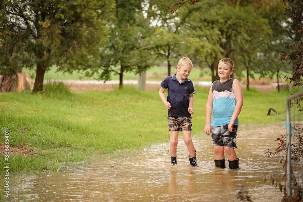 Obraz premium Two young brothers playing in flooded creek wearing gumboots in water