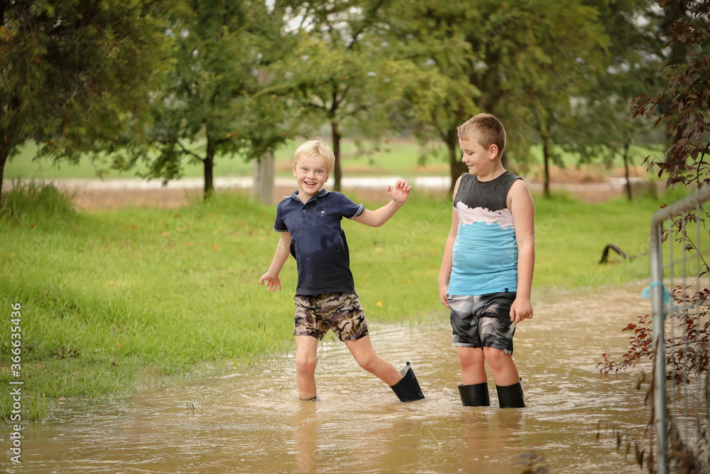 Boys playing in flooded creek with wet gumboots Boys playing in flooded creek with wet gumboots
