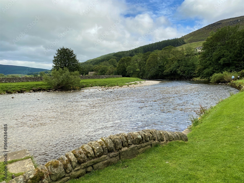 The river Wharfe, as it flows past the village of Burnsall, with trees and hills in the distance in, Burnsall, Skipton, UK