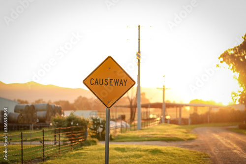 Yellow causeway sign on country road at sunset photo