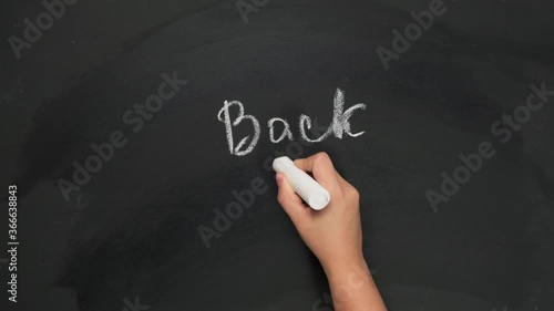 female hand holds white chalk and writes back to school on black chalk board, start of the school year