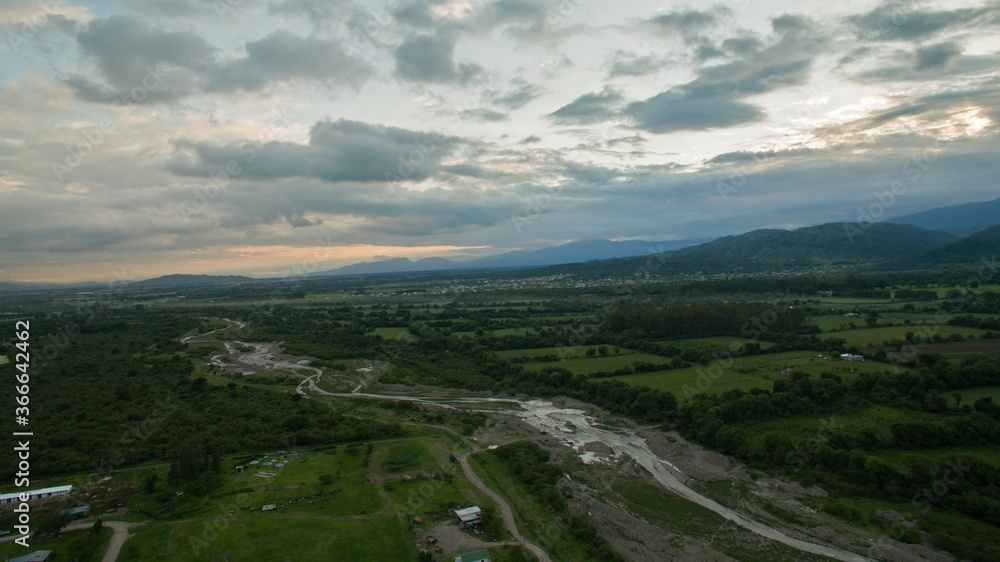 Naklejka premium Rural landscape. Aerial view of the countryside. The river flowing across the plantation fields, forest and mountains at sunset. 