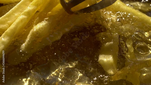 French fries. Finger chips. Close up. .Frying and stirring potato strips in hot boiling sunflower oil..Concept of homemade food and cooking..Concept of unhealthy, greasy fast food.