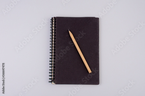 Top view of closed black cover notebook with pencil on white desk background