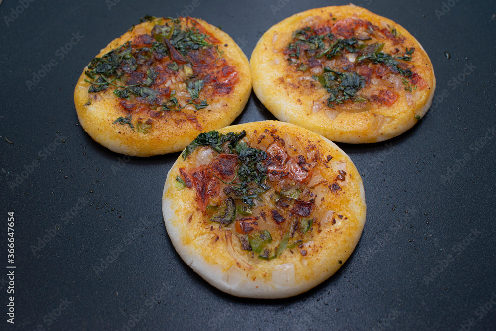 top view of three mini round( circular) utappam on hot black non tick tawa or pan top view of three mini round( circular) utappam on hot black non tick tawa or pan