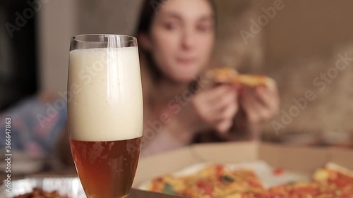 The girl eats pizza, drinks beer and puts the glass back on the table. Blurred background. Selective focus