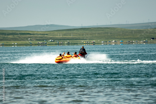 A jet ski pulls an inflatable raft with people on the water. A fun adventure at speed. © Vectorina