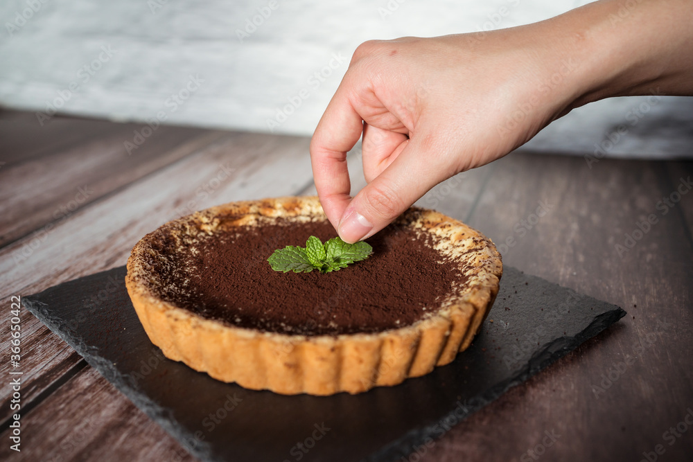 A top view of a delicious chocolate tart with mint on top being prepared by hand