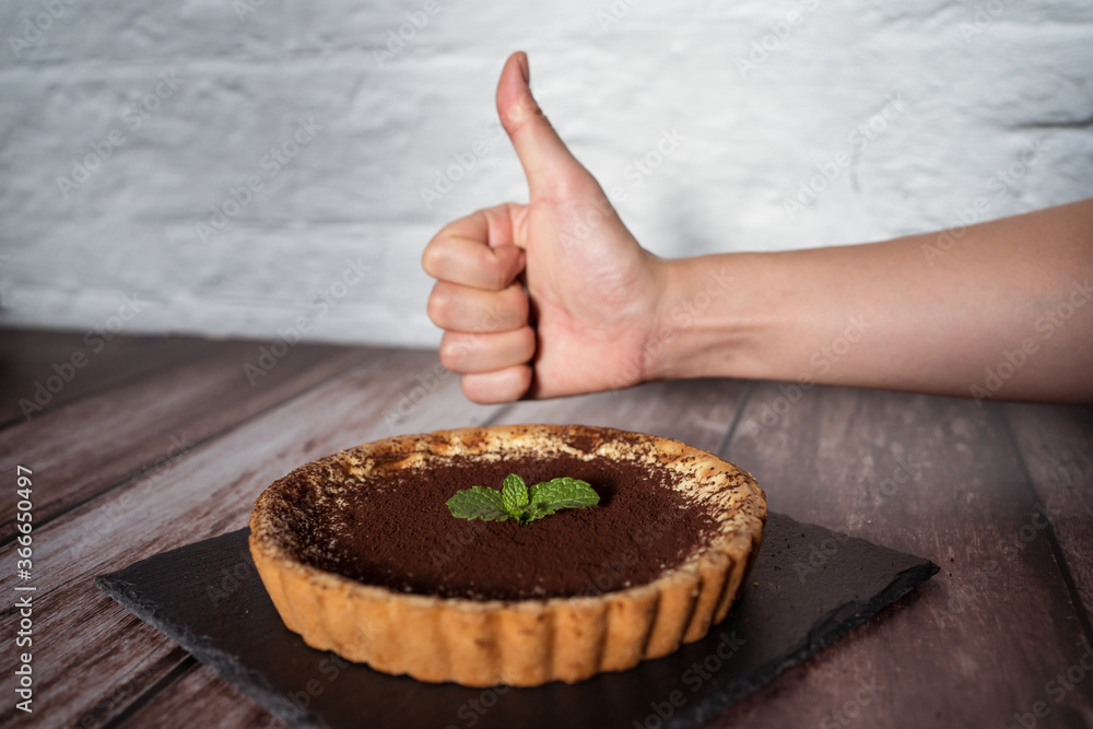 A top view of a delicious chocolate tart with mint on top being prepared by hand