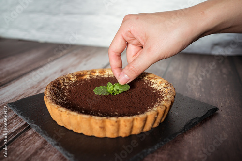 Obraz na płótnie A top view of a delicious chocolate tart with mint on top being prepared by hand w salonie