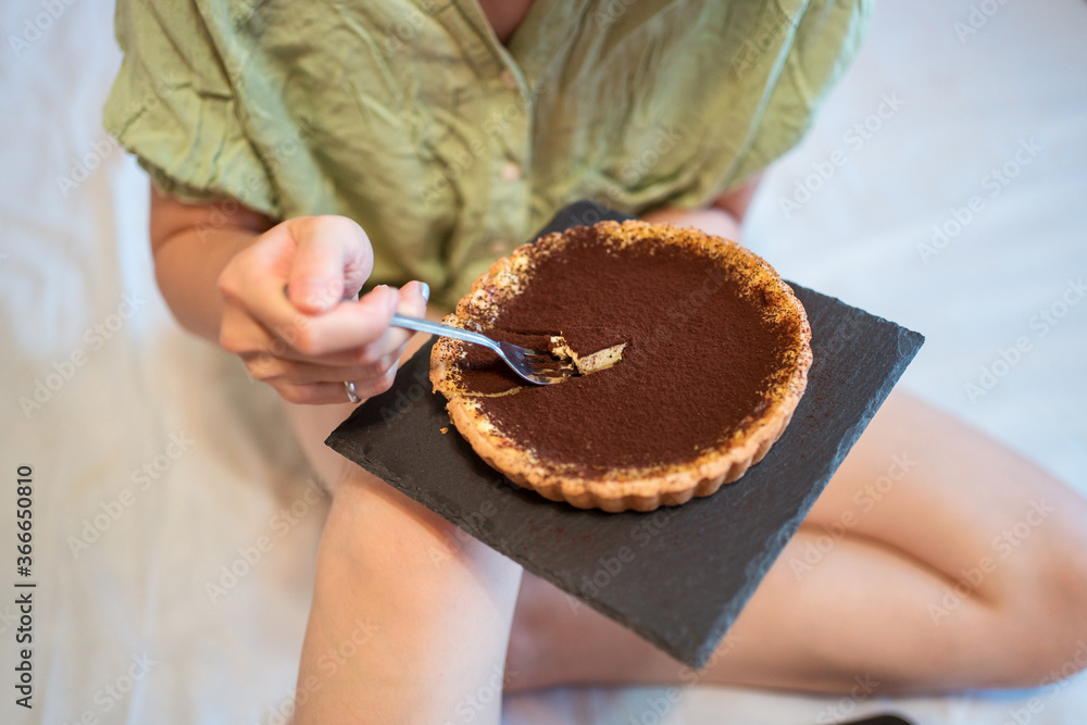 A top view of young pretty Asian woman eating delicious chocolate tart on bed