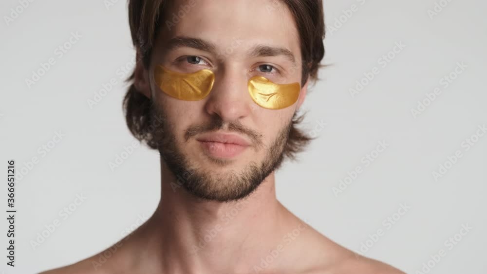 Close up attractive bearded man with gold patches under eyes confidently posing on camera over white background Close up attractive bearded man with gold patches under eyes confidently posing on camera over white background