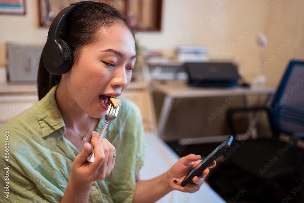 Young pretty Asian woman eating delicious chocolate tart on bed