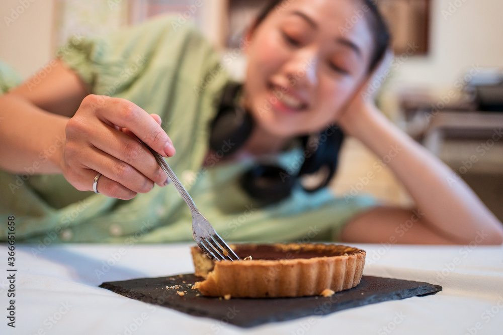 Young pretty Asian woman eating delicious chocolate tart lying on bed