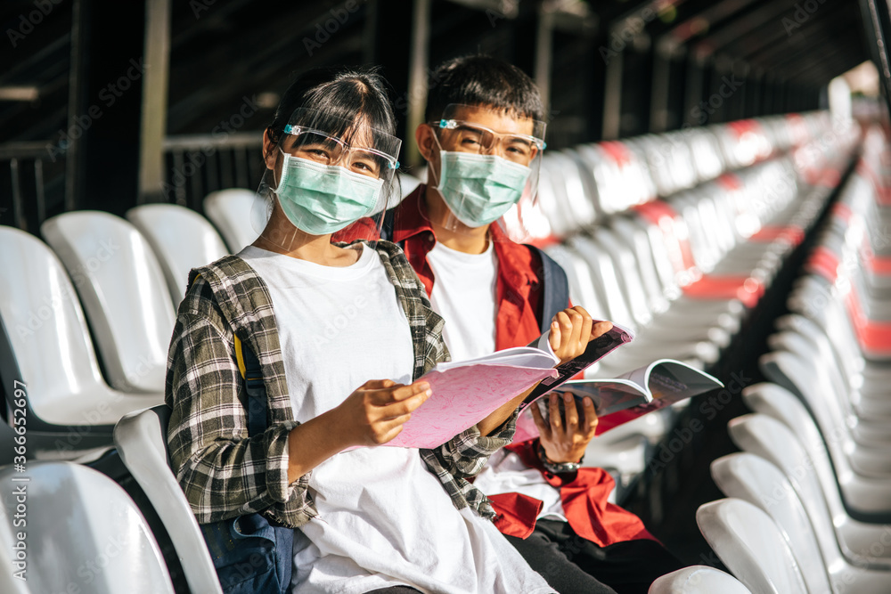 Male and female students wear masks and sit and read on the field chair