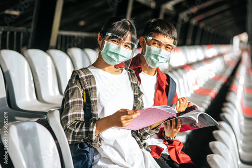 Male and female students wear masks and sit and read on the field chair
