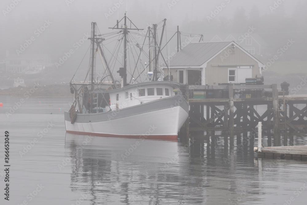 Fototapeta premium Calm, restful scene in coastal Maine. Fishing trawler anchored alongside dock and enveloped in thick fog at picturesque fishing village of Port Clyde.