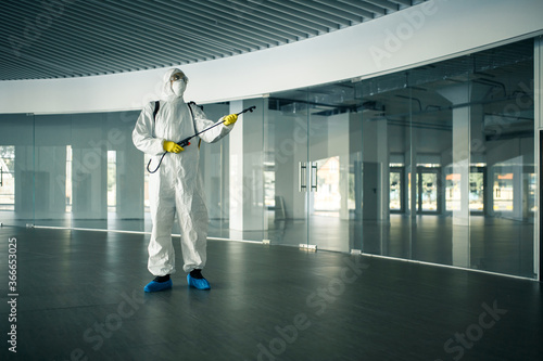 A man wearing disinfection suit spraying with sanitizer the glass doors' handles in an empty shopping mall to prevent covid-19 spread. Health awareness, clean, defence concept. © Konstantin Zibert
