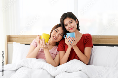 Happy Couple asia woman enjoy together with drink morning coffee, fresh tea or hot milk in cup on the bed in morning.