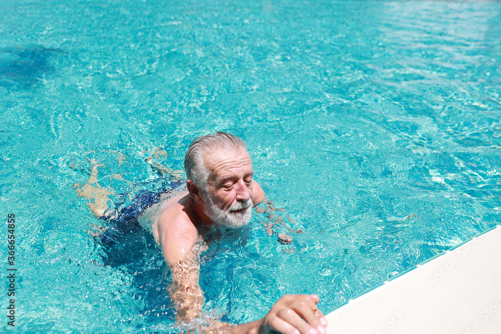 happy elderly caucasian swimming in pool during retirement holiday with relaxation and smiling