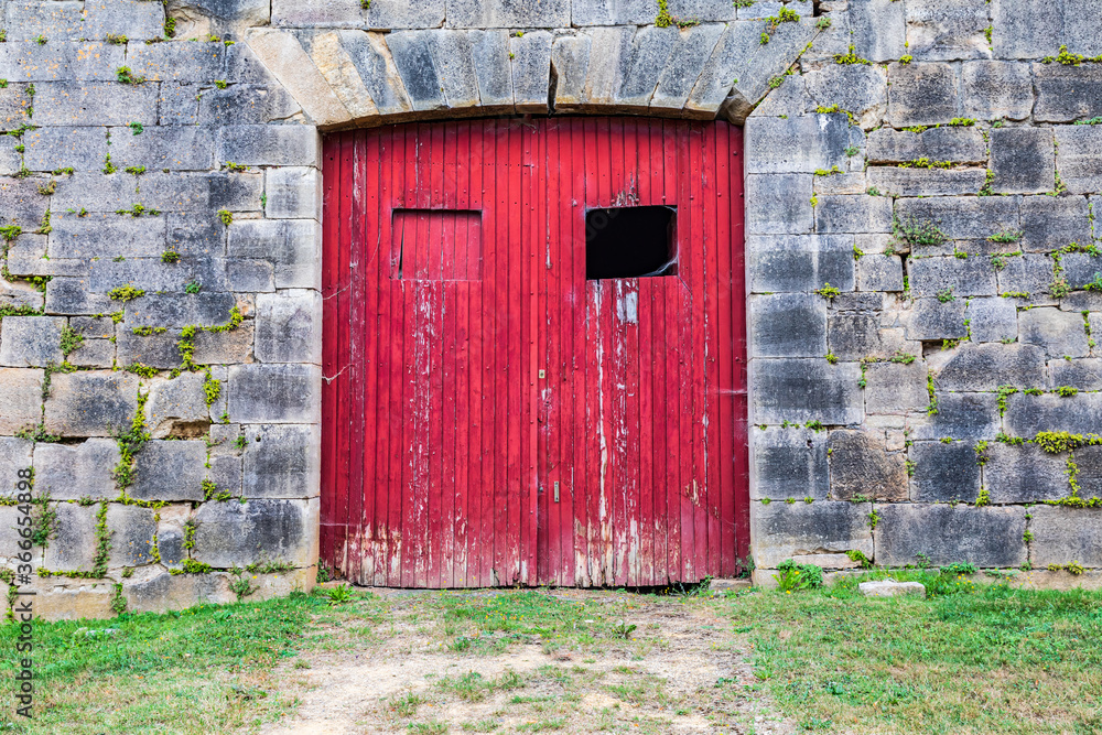 Red door in a stone wall in the town of Hautefort.
