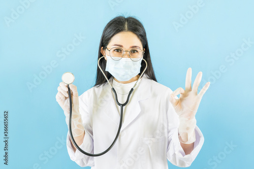Smart young asian female doctor in lab coat with Medical face mask white latex medical gloves and stethoscope against blue background health care concept