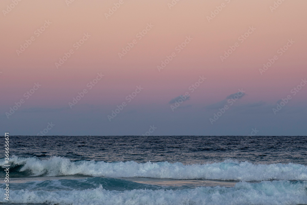 Obraz premium sunset over the sea. Small waves breaking on beach below beautiful pink coloured sunset
