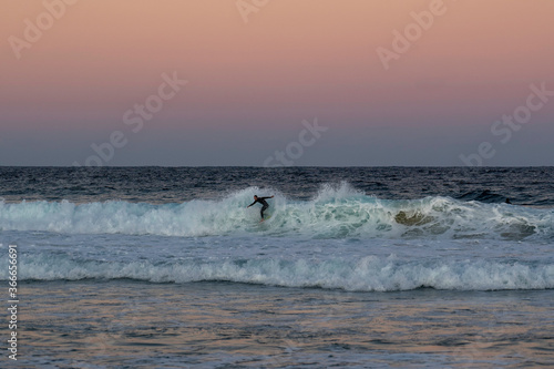 "Maroubra Beach, NSW / Australia - 5th July 2020" Surfer catching waves at sunset, beautiful pink coloured sunset © Em Neems Photography