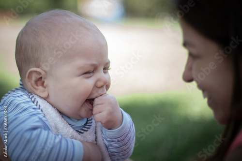 Bebé varón con su mamá en un parque riendo y sonriendo mirándose uno al otro photo