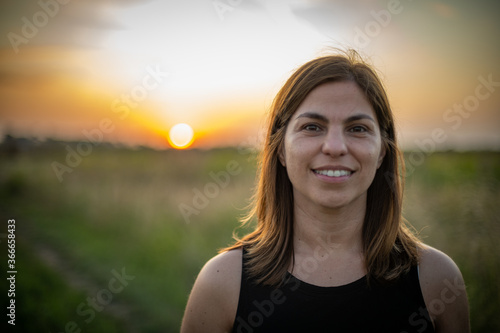 Mujer sonriendo al atardecer o amanecer en campo de Argentina con árboles de fondo photo