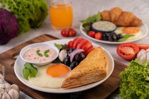 Breakfast consists of bread, fried egg, salad dressing, black grapes, tomatoes, and sliced ​​onions.