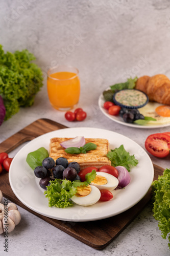 Breakfast consists of bread, boiled eggs, black grape salad dressing, tomatoes, and sliced ​​onions.