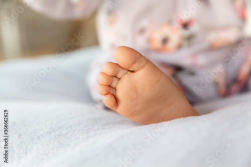 Adorable infant foot on soft blanket at natural light, babyhood concept