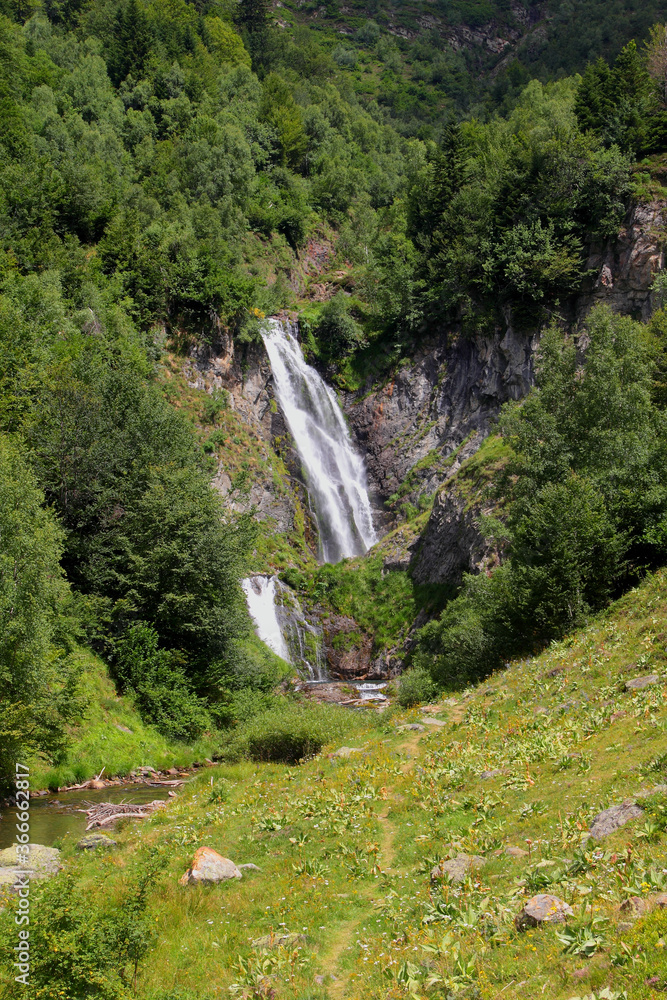 A relaxing summer landscape with waterfall and leafy trees on mountain route