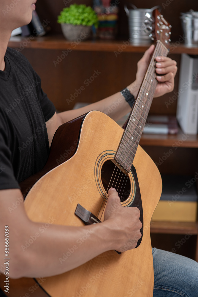 Obraz premium A man sitting and playing guitar on a chair.