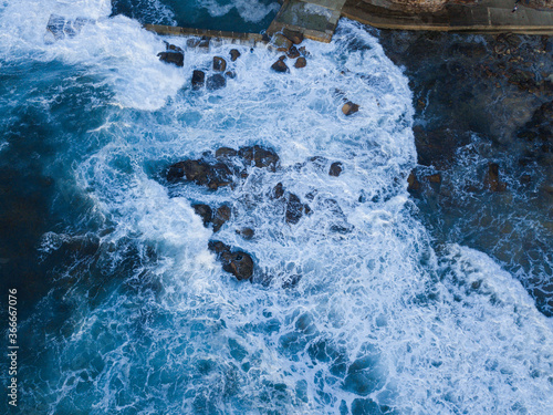 Top down aerial view of wave flowing around rocks.