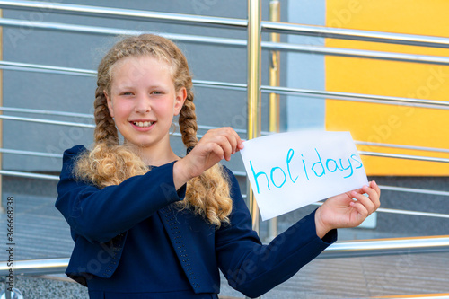 happy girl holding  paper with the words holidays. Concept School holidays,graduation.  girl in a  uniform. pupil, learner, scholar. happy schoolgirl photo