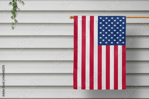 United States national small flag hangs from a picket fence along the wooden wall in a rural town. Independence day concept.