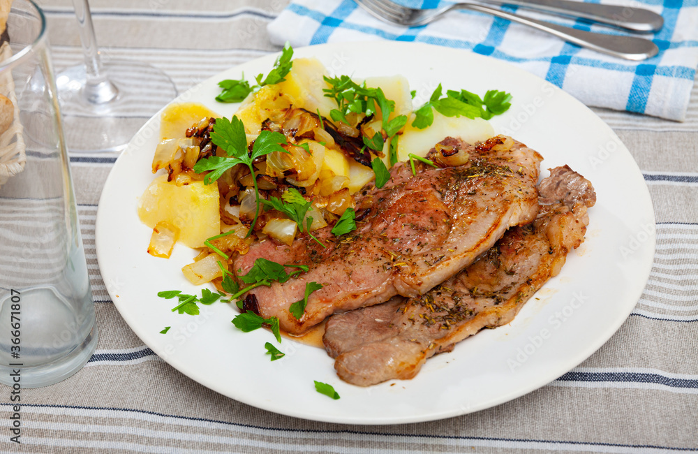 Juicy pork chops with vegetable garnish of boiled potato, fried onion and chopped fresh parsley