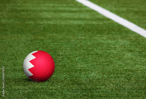 Bahrain flag on ball at soccer field background. National football theme on green grass. Sports competition concept.