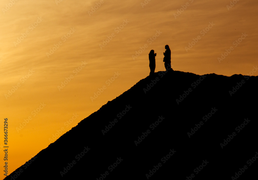 People stand on top of a steep hill on a sunset background. Beautiful sunset sky and silhouettes