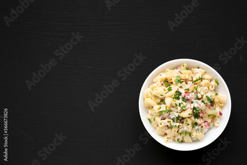 Homemade Macaroni Salad in a white bowl on a black background, top view. Flat lay, overhead, from above. Copy space.