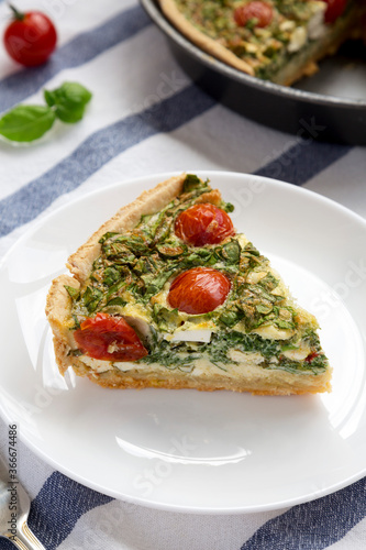 A Piece of Homemade Spinach Quiche on a white plate, side view. Close-up.