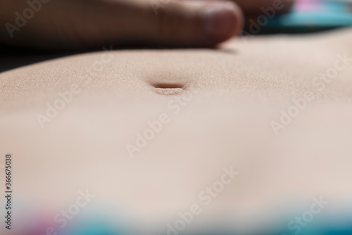 Stomach of young woman in lying and sunbathing in sunny summer day. Personal perspective