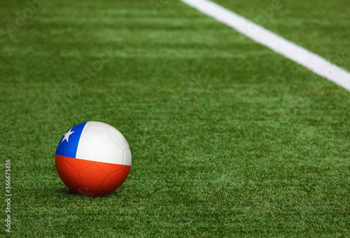 Chile flag on ball at soccer field background. National football theme on green grass. Sports competition concept.
