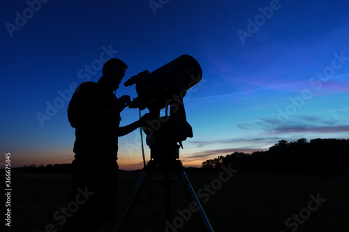 silhouette of a man setting up a telescope for night observation on dark blue sky at dusk photo